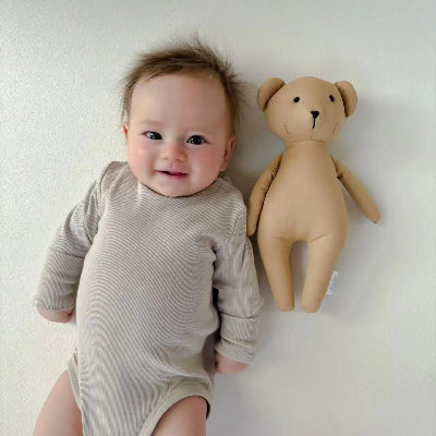 un sourire radieux avec son doudou ourson beige tout près
