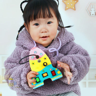 Tout petit tient le Tableau Montessori BusyBoardCircuit™ fusée d'une seul main.