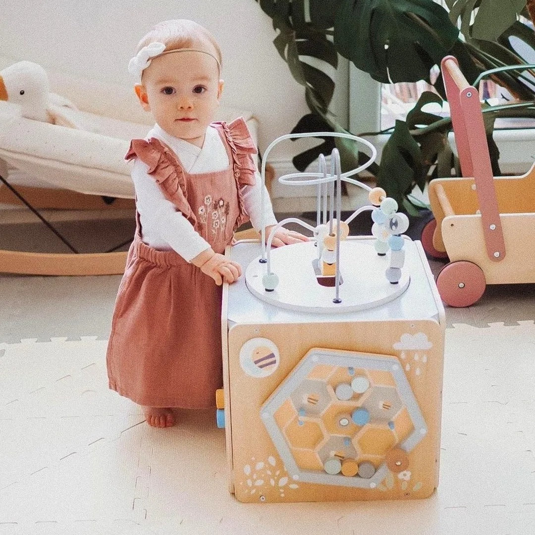 Bébé à peine debout, essaye de manipuler le cube de motricité 