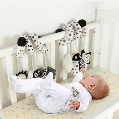 Bébé essai d'attraper un des hochets noir et blanc de sa pirale d'activité enroullé au berceau