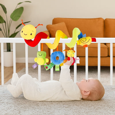 Bébé sur le dos fournit un effort de motricité pour essayer d'atteindre la  Spirale d'activité enroulé au lit.