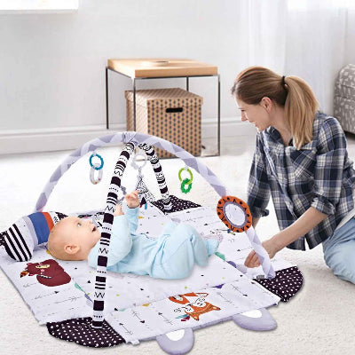 Maman observe avec joie l'interaction de son bou de chou sur le dos avec l'ensemble des jouets suspendu au tapis d'éveil bébé