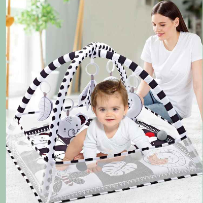 Maman tout apaisé, observe son Bou de Chou essayer de se mettre sur ses genoux pour atteindre les jouets suspendus du tapis d'éveil bébé