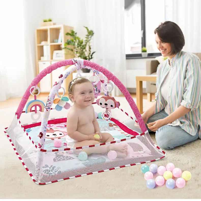 Maman toute souriante, observe sa fille interagir de façon autonome avec les jouets suspendus du tapis d'éveil bébé